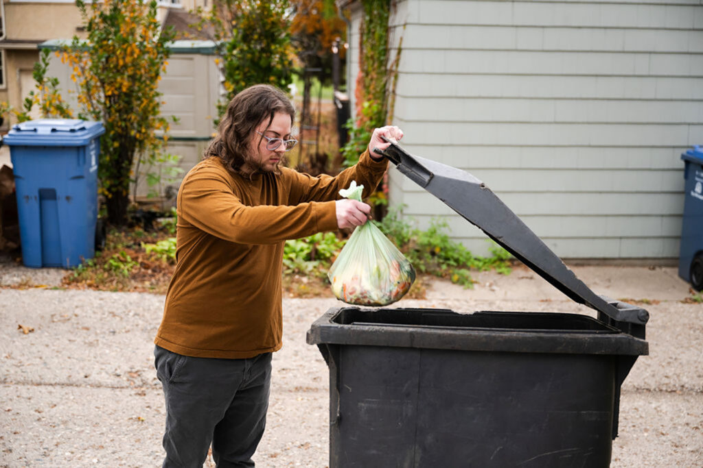 Person dropping filled food scraps bag in trash cart