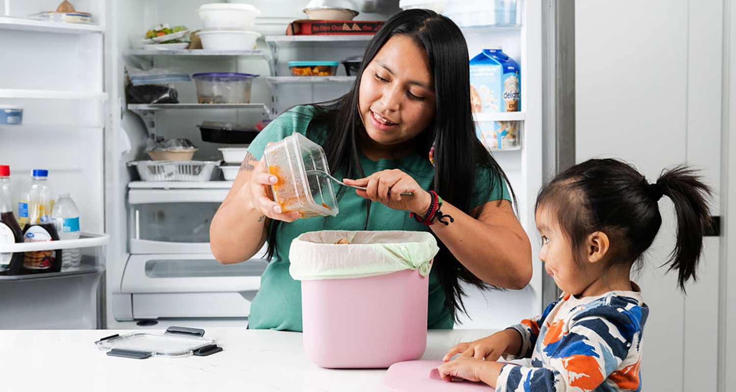 Parent and child in kitchen filling food scraps bag